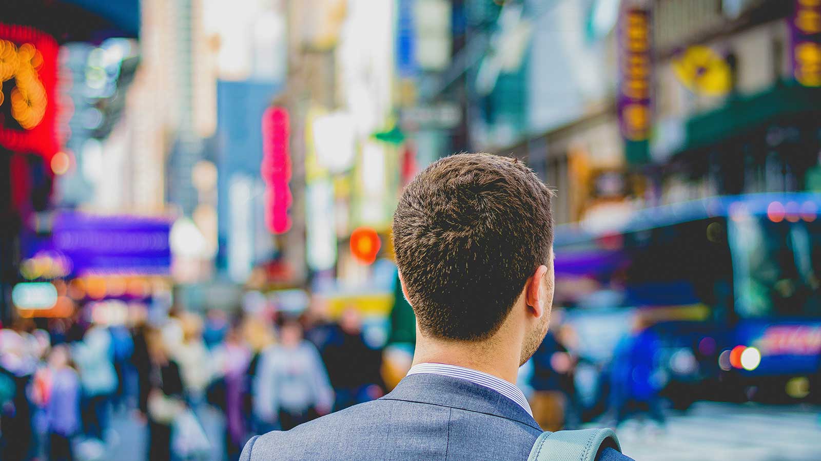 If We Do Not Fix Immigration, Canada May Solve the Problem for Us. img showing a man dressed in a suite from the back with blurry background of busy street with people